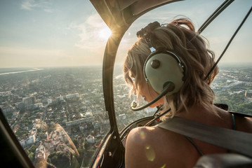 Portrait of beautiful blonde women enjoying helicopter flight. She is amazed by cityscape. - obrazy, fototapety, plakaty