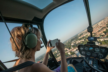 Beautiful blonde women taking photo of cityscape with smart phone in helicopter.