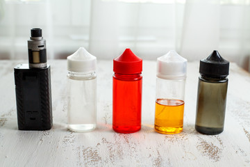 Vape objects. Electronic cigarette and jars with e-liquid on a light wooden table.