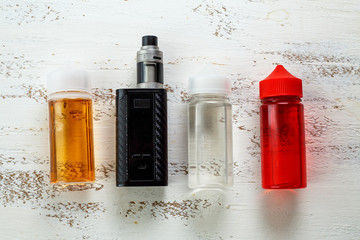 Vape objects. Electronic cigarette and jars with e-liquid on a light wooden table.