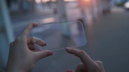 Busy female hands tapping swiping on virtual transparent touchscreen using a futuristic smartphone outdoors in the city at sunset. - Powered by Adobe