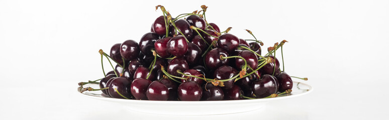 panoramic shot of fresh, sweet, red and ripe cherries on white plate
