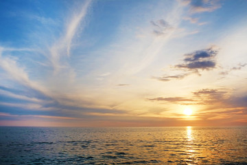 Fototapeta na wymiar Beautiful seascape of sun setting over calm azure water with wind patterns and clear blue orange gradient sky without clouds. Ocean view with horizon, background with a lot of copy space for text.