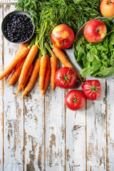Variety of fresh fruits, vegetables and berries carrot, spinach, tomatoes, red apples, blueberries over white plank wooden background. Flat lay, space