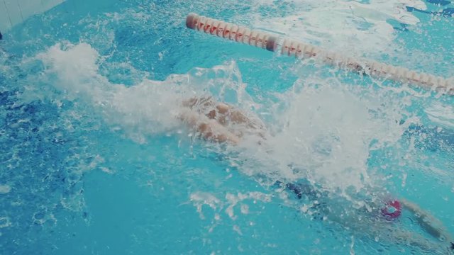 Powerful strong young woman swim backstroke style, she push off from the pool, floating underwater, and reaching high speed. A lot of water splash and waves. Super slow motion