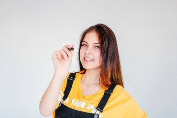 Young smiling girl student worker with dark long hair in yellow t-shirt with graphic pen in hand, isolated on grey background