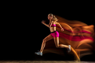 Professional female relay racer training isolated on black studio background in mixed light. Woman...