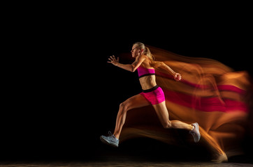 Fototapeta na wymiar Professional female relay racer training isolated on black studio background in mixed light. Woman in sportsuit practicing in running. Healthy lifestyle, sport, workout, motion, action concept.