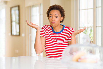 Young beautiful african american woman at home clueless and confused expression with arms and hands...