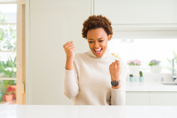 Young beautiful african american woman at home very happy and excited doing winner gesture with arms raised, smiling and screaming for success. Celebration concept.
