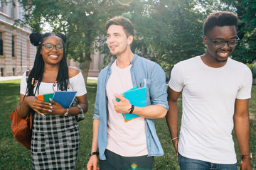 Group of cheerful students with backpack holds books walking at the campus outdoors, close up. Youth Friendship Together Smiling Happiness Concept. Sun glare effect