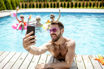 Handsome man takng selfie photo with phone, while resting in the swimming pool with friends...