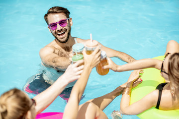Group of a happy friends having fun with drinks while swimming in the water pool outdoors during the summertime