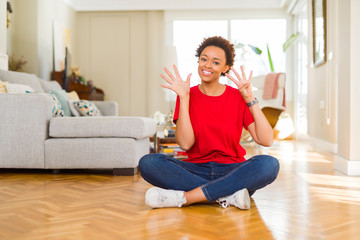 Young beautiful african american woman sitting on the floor at home showing and pointing up with fingers number nine while smiling confident and happy.