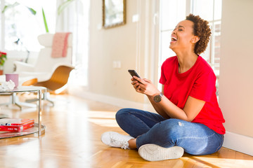 Obraz premium Beautiful young african american woman sitting on the floor using smartphone smiling