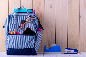 Backpack with different colorful stationery on wooden table. Back to school.
