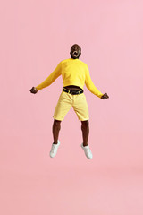 Fototapeta na wymiar Jump. Black man jumping in air and screaming on pink background