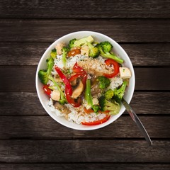 Risotto in a bowl with fried vegetables, mushrooms and tofu on the table. Rice, peppers, broccoli, champignons and tofu is a tasty and healthy dish.