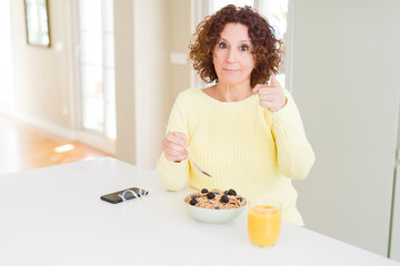 Obraz na płótnie Canvas Senior woman eating healthy breakfast in the morning at home pointing with finger to the camera and to you, hand sign, positive and confident gesture from the front