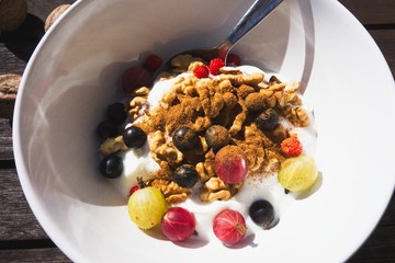 Healthy, sweet, colorful and low-carbohydrate breakfast in a bowl with walnuts, fresh fruit (strawberries, gooseberries, currant), yoghurt and a cinnamon. Vegetarian food. Closeup, authentic photo.
