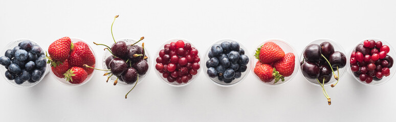 panoramic shot of fresh and ripe strawberries, blueberries, cherries and cranberries in plastic cups