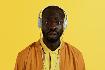 Surprised man in headphones listening music on yellow background