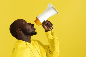 Attention! Black man shouting in megaphone on yellow background