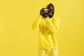 Happy man in colorful clothes with photo camera on yellow