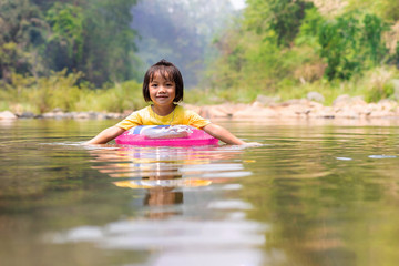 Little Asian girl with pool ring floating in river