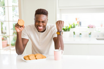 African american man eating healthy whole grain biscuit screaming proud and celebrating victory and success very excited, cheering emotion