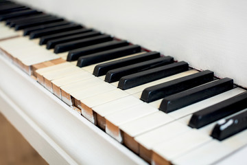 Keys of an old white piano with peeling paint close up