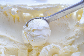 Ice cream scooping out of container by metal spoon close up