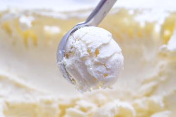 Ice cream scooping out of container by metal spoon close up
