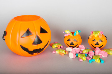 Happy Halloween Trick or Treat jack-o-lantern buckets and pile of colorful sweets candy on gray background. Plastic pumpkins  to collect candy.