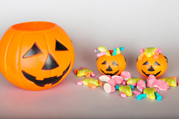 Happy Halloween Trick or Treat jack-o-lantern buckets and pile of colorful sweets candy on gray background. Plastic pumpkins  to collect candy.