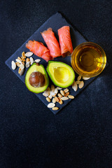 Selection of healthy fat sources, avocado, salmon, nuts, olive oil on a black plate. The concept of healthy eating. Top view, copy space, black background