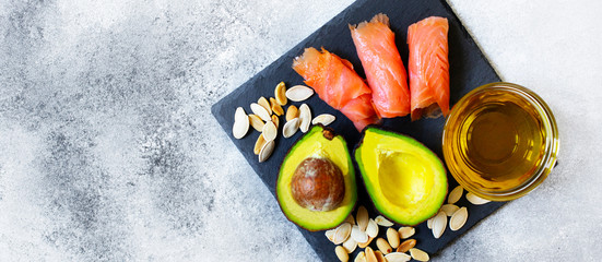 Selection of healthy fat sources, avocado, salmon, nuts, olive oil on a black plate. The concept of healthy eating. Top view, copy space, gray background