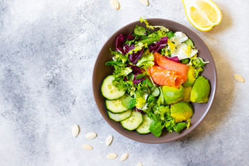 Healthy dietary salad with salmon, avocado, pumpkin seeds, fresh vegetables and lemon. The concept of healthy eating. Gray background, top view, copy space