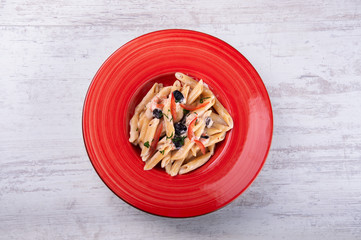 Penne pasta with olive in a red plate, on white wood background