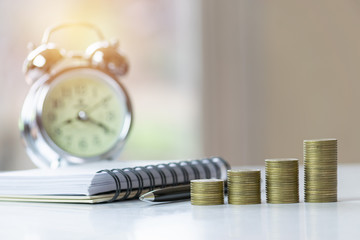 Coins with clock and notebook on table for business,finance,save concept.