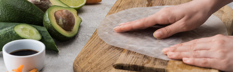 panoramic shot of woman putting rice paper on cutting board among ingredients