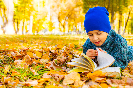 Boy Lying On His Stomach Reading A Book In The Fall In The Park