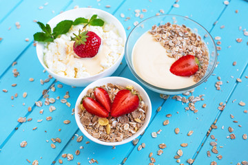Yogurt, muesli and cottage cheese in white plates stand on a blue wooden background in the center of the frame