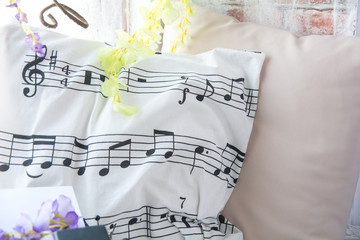 Pillow with musical notes on the windowsill with flowers. Brick wall background with artificial flowers