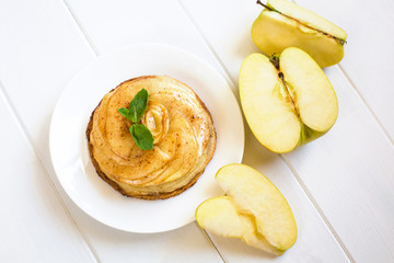 On a white plate lies a cake of apple charlotte with mint leaves close-up on a white wooden...
