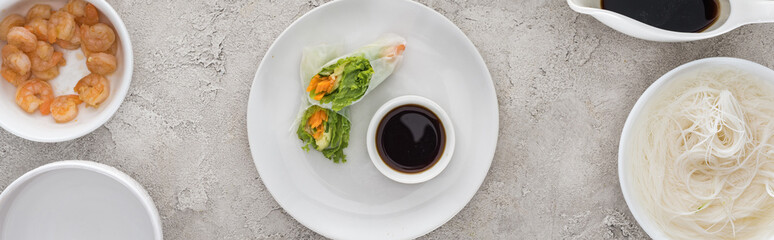 panoramic shot of tasty and served spring rolls with soy sauce on white plate