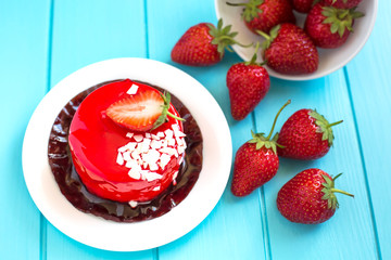 Red round cake with strawberry souffle, decorated with mint leaves on a plate, which stands on a...