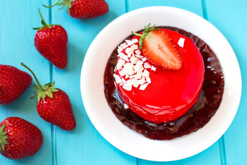 Red round cake with strawberry souffle, decorated with mint leaves on a plate, which stands on a blue wooden background. Nearby are strawberries.