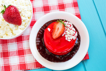 Red round cake with strawberry souffle, decorated with mint leaves on a plate, which stands on a blue wooden background. Nearby is a plate with cottage cheese