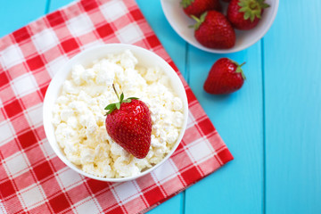 Fresh tasty granular cottage cheese with strawberries in a white deep plate on a blue wooden background and a red-tinted cotton towel